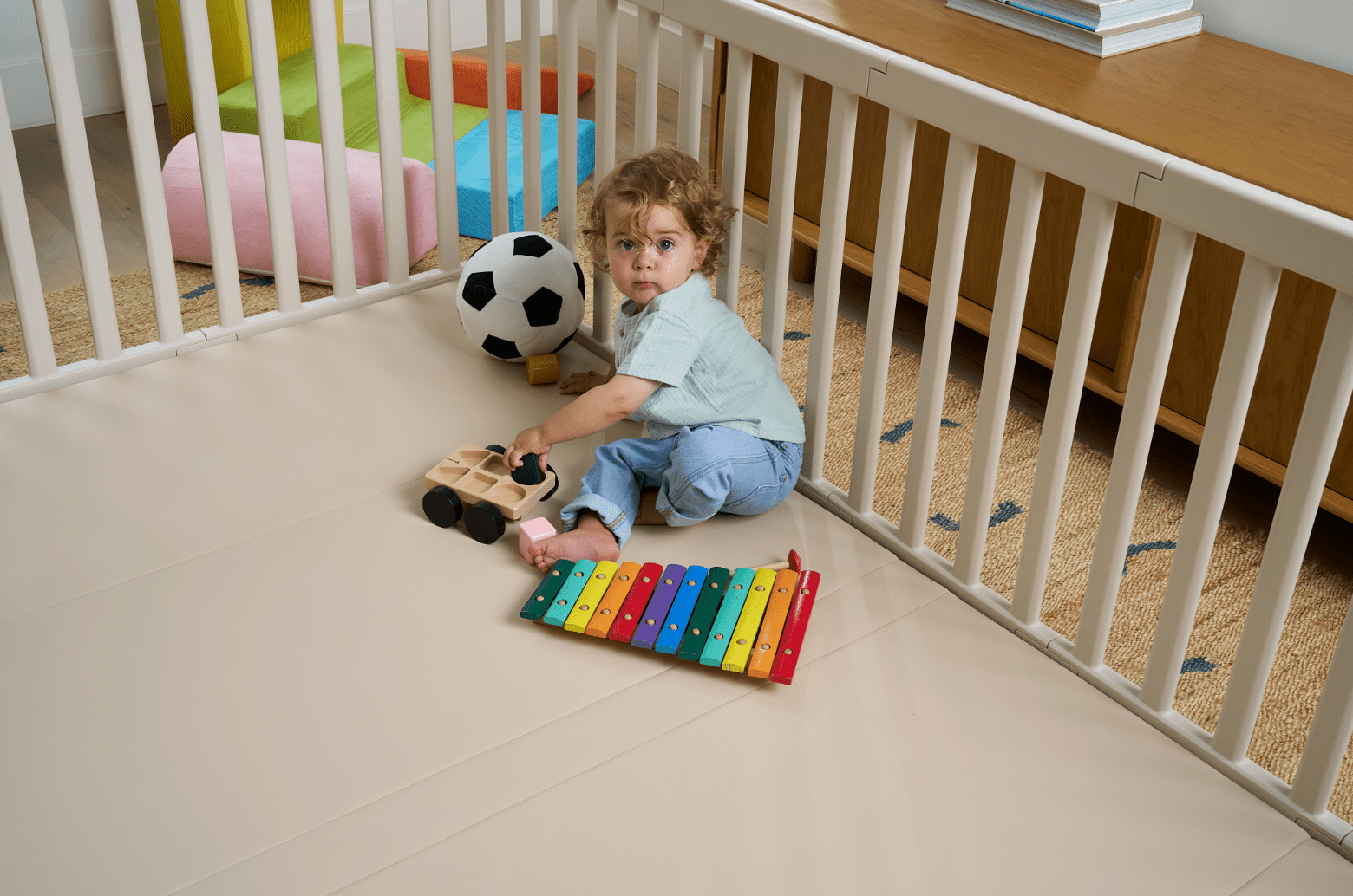 Baby enjoying independent play inside a soft play mat and playpen set in a modern living room play area