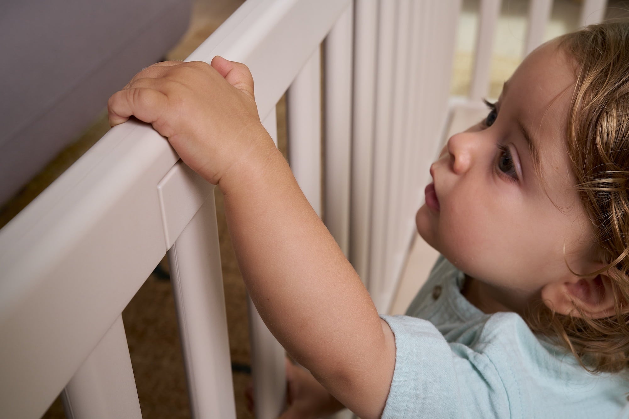 Child safely holding rounded railing of Matty’s Room white baby playpen