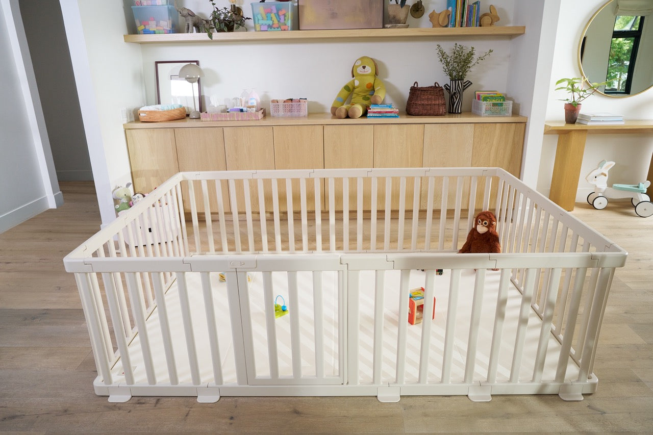 White baby playpen and cushioned play mat system in a modern living room with toys inside