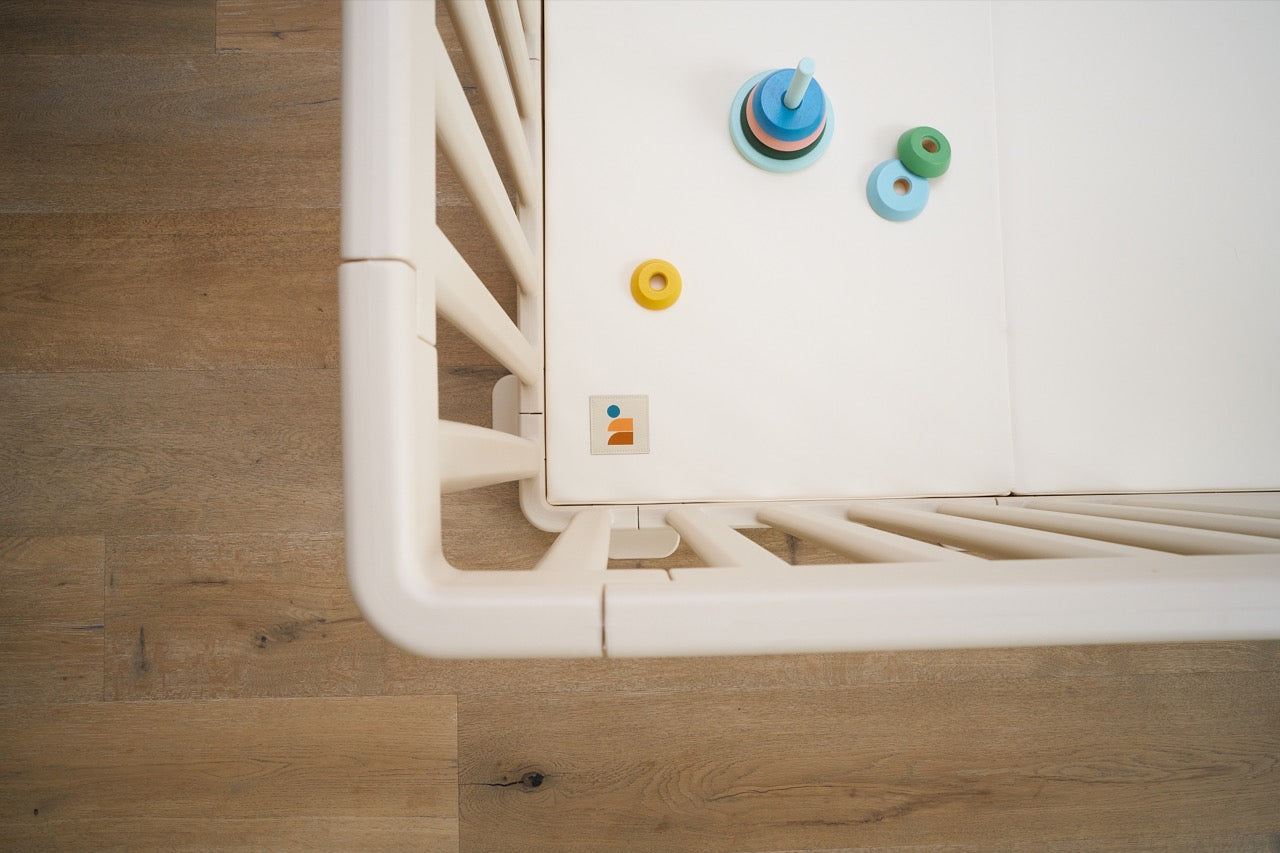 Overhead view of white baby playpen and playmat system with toys inside