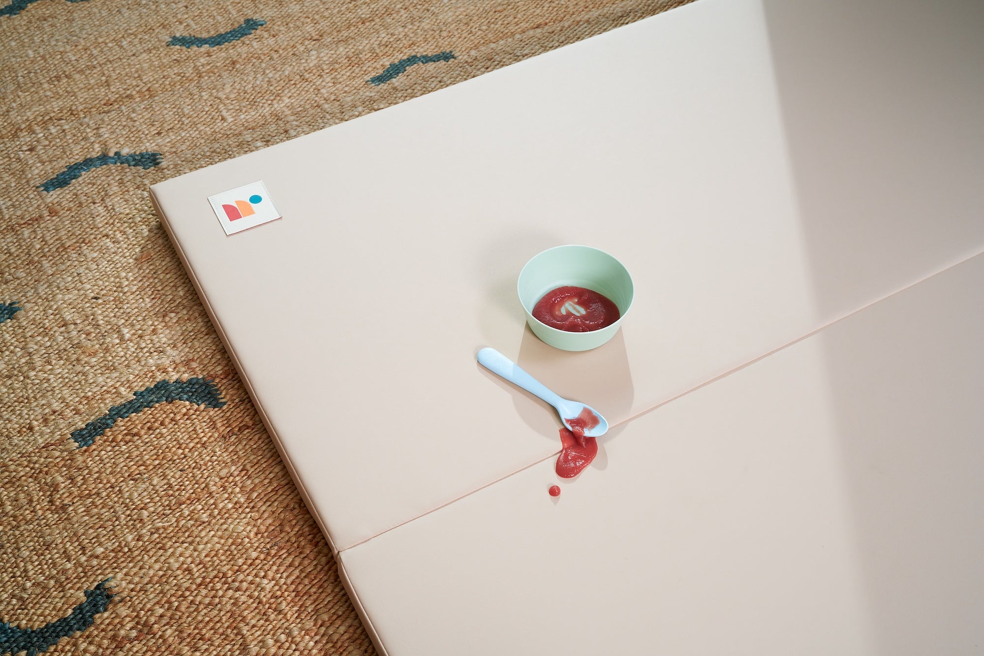 Red baby food spilled on taupe cushioned baby playmat surface